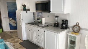 Ett kök med vita skåp, ett kylskåp i rostfritt stål, en mikrovågsugn, en mixer och en kaffebryggare.