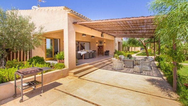 Um pátio moderno ao ar livre com churrasqueira, área de estar e uma seção coberta com pérgola.