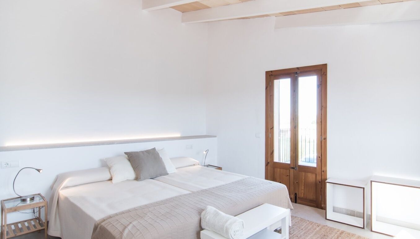 A bedroom with a large bed, bedside tables, a wooden door, and a small desk.