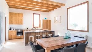Eine moderne Küche mit Holzschränken, einer zentralen Kochinsel mit Hockern und einem Esstisch mit Stühlen.