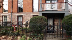 Un edificio de ladrillo con una verja metálica negra, un pequeño jardín y una estatua de un águila.