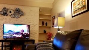 Una sala de estar con un sofá de cuero, un televisor de pantalla plana, una chimenea, detalles decorativos en la pared y una estantería.