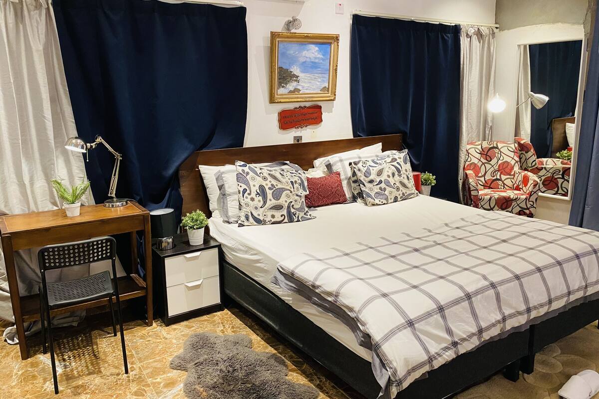 Een keurig opgemaakt slaapkamer met een bed, nachtkastje, lamp, stoel en een kleine potplant.