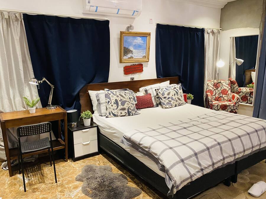 A neatly arranged bedroom with a bed, bedside table, lamp, chair, and a small potted plant.