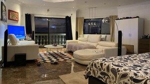 Een moderne hotelkamer met een bank, een bed, een televisie, een kledingkast en een balkon met uitzicht.