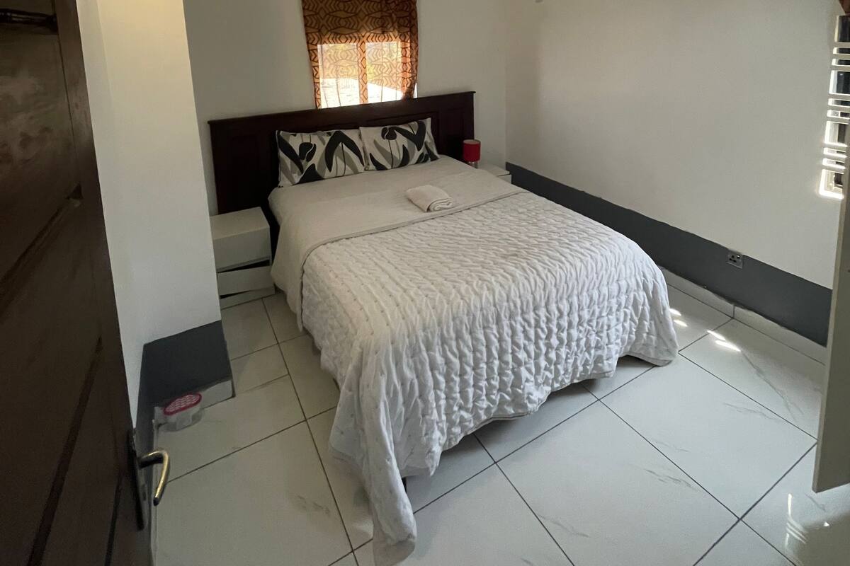 Een slaapkamer met een bed, een plafondlamp, een airconditioner en een raam met gordijnen met een patroon.