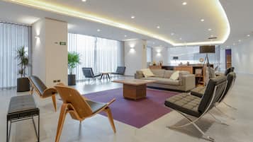 A modern hotel lobby with a seating area, a reception desk, and a large window.