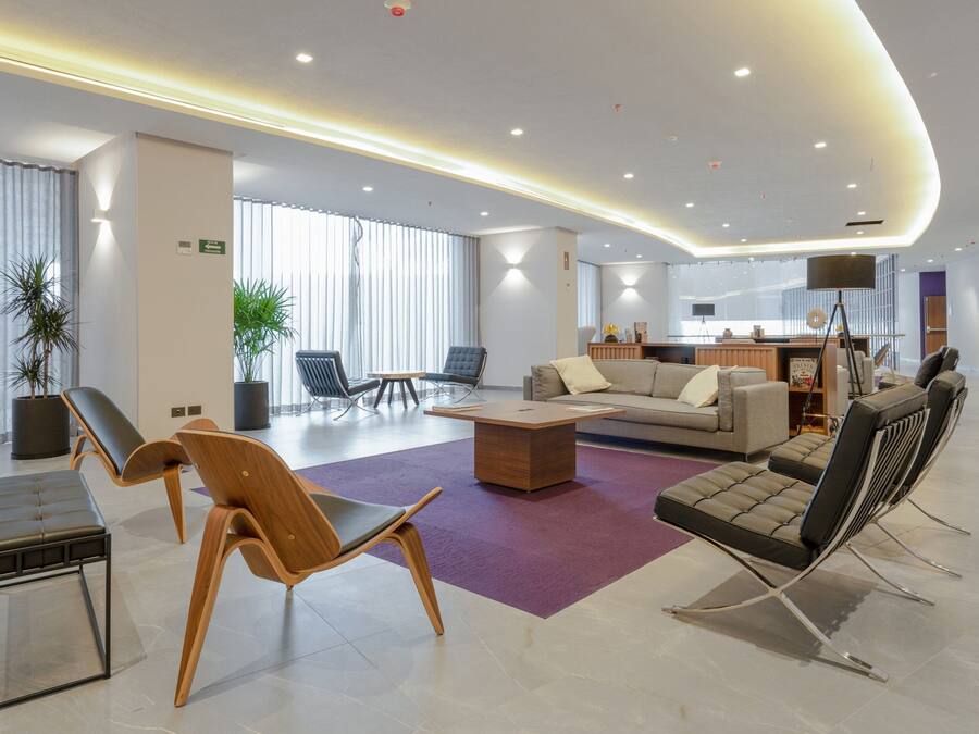 A modern hotel lobby with a seating area, a reception desk, and a large window.