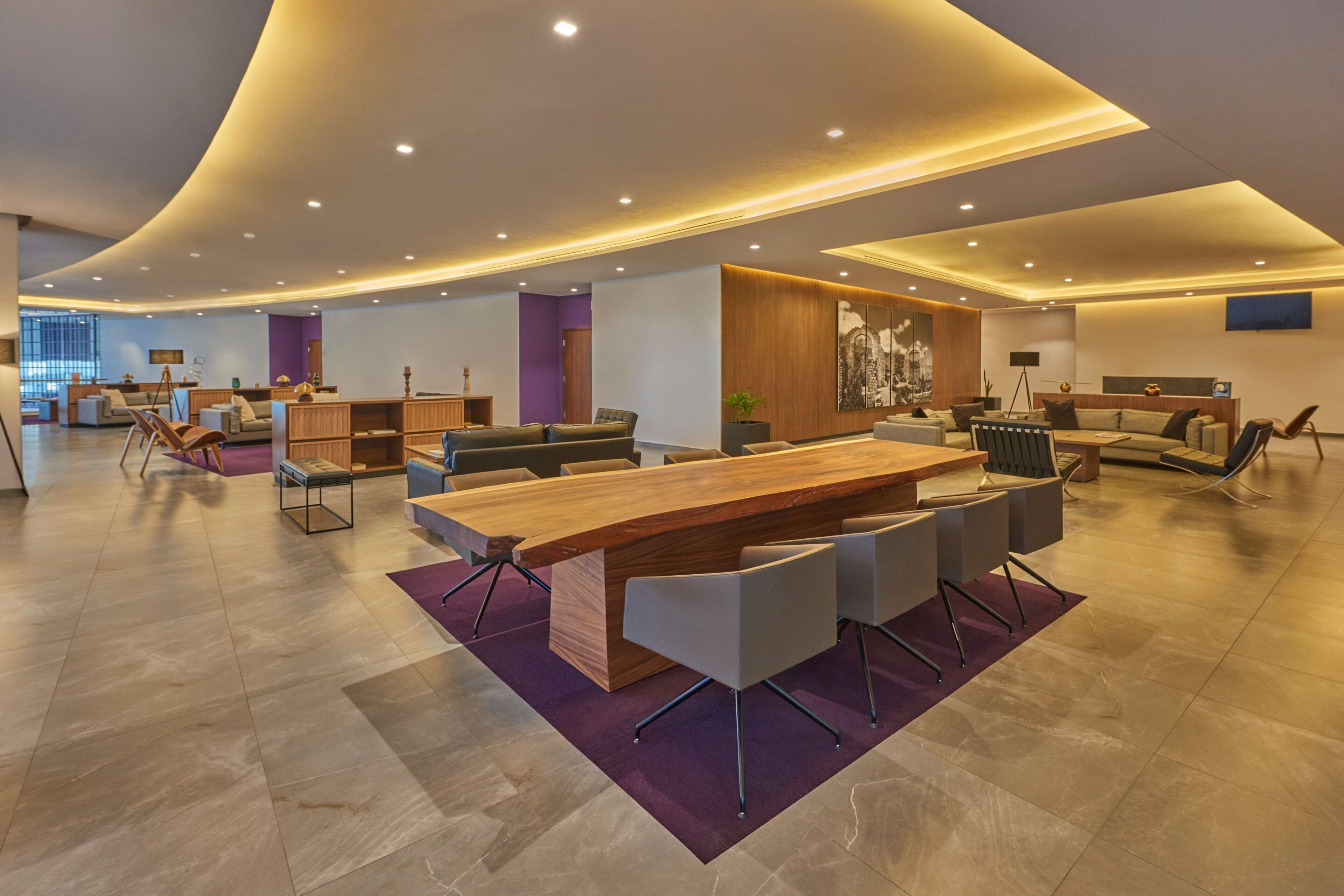 Une salle de conférence spacieuse et moderne, dotée d’une grande table en bois, de sièges confortables et d’un plafond bien éclairé grâce à des luminaires encastrés.
