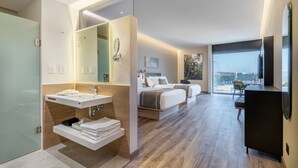 Una habitación de hotel moderna con baño, cama, escritorio y un amplio ventanal con vistas a la ciudad.