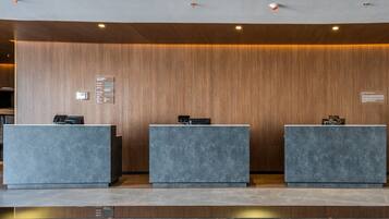 A reception area with three grey reception desks against a wooden wall, equipped with a digital information board and a small clock.