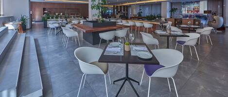 Un restaurante moderno con una barra central, diversas opciones de asientos y una variedad de plantas.