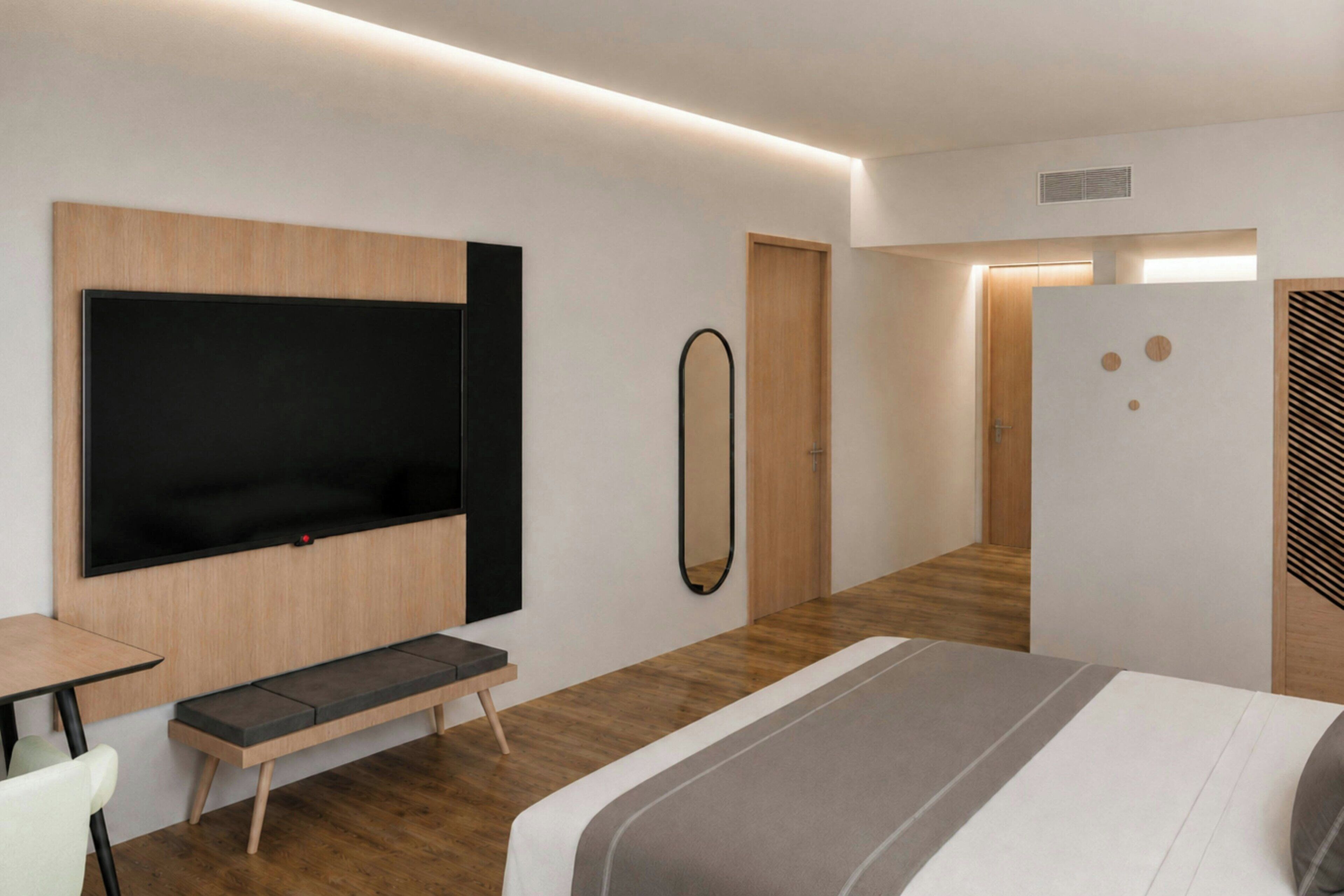 Una habitación de hotel moderna con cama, zona de estar, televisor y espejo.