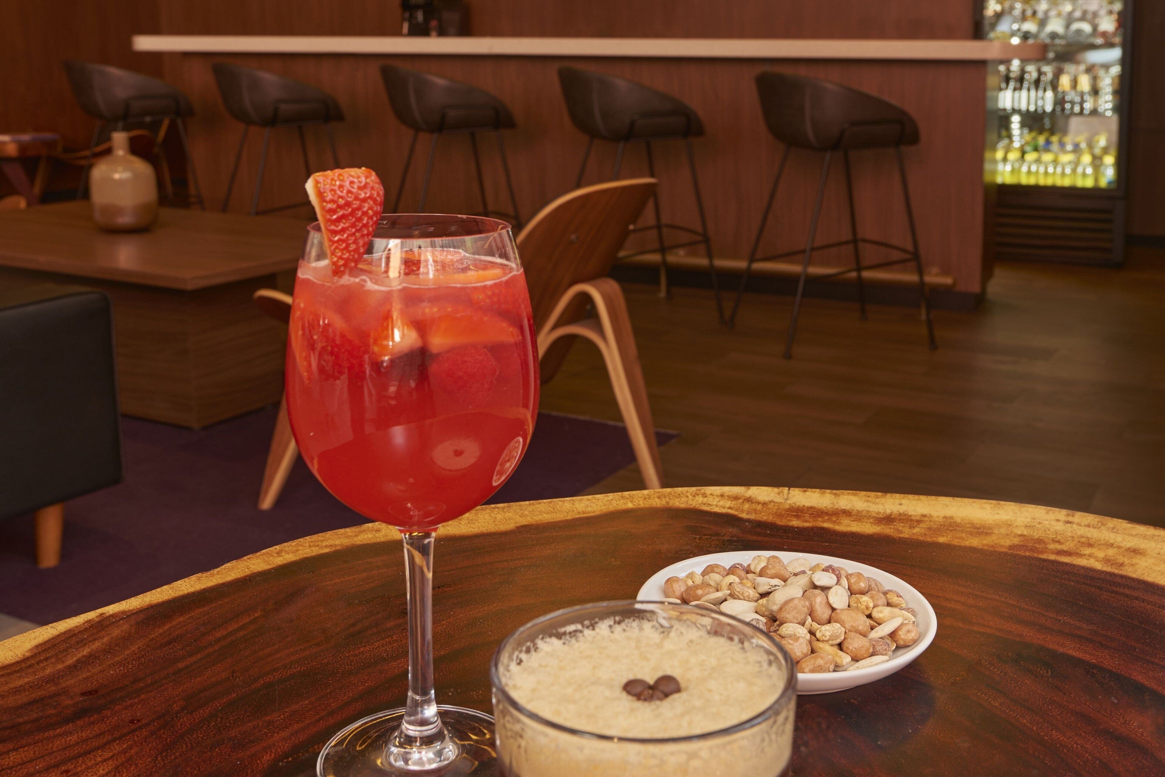 A bar area with a drink, a bowl of nuts, and a dessert on a wooden table.