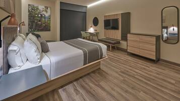 Een moderne hotelkamer met een groot bed, een bureau met stoel, een klein tafeltje, een televisie, een dressoir en een schilderij aan de muur.