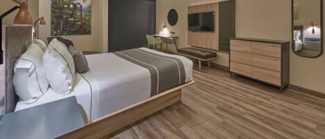 A modern hotel room with a large bed, a desk with a chair, a small table, a TV, a dresser, and a painting on the wall.