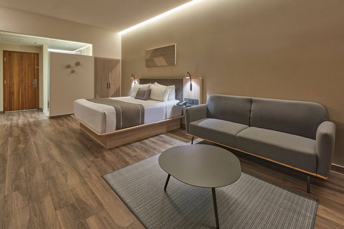 Une chambre d’hôtel moderne avec un lit, un canapé, une petite table et un plancher en bois.