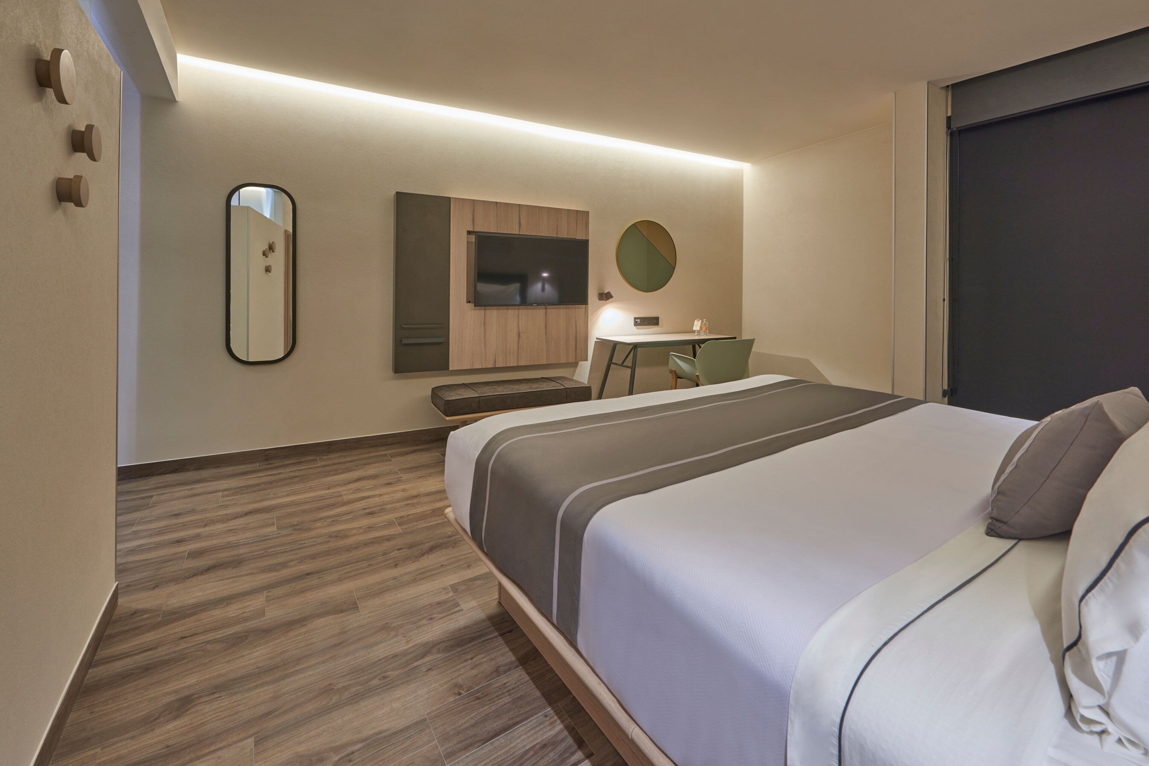 A modern hotel room with a large bed, a desk, a chair, a TV, and a mirror.