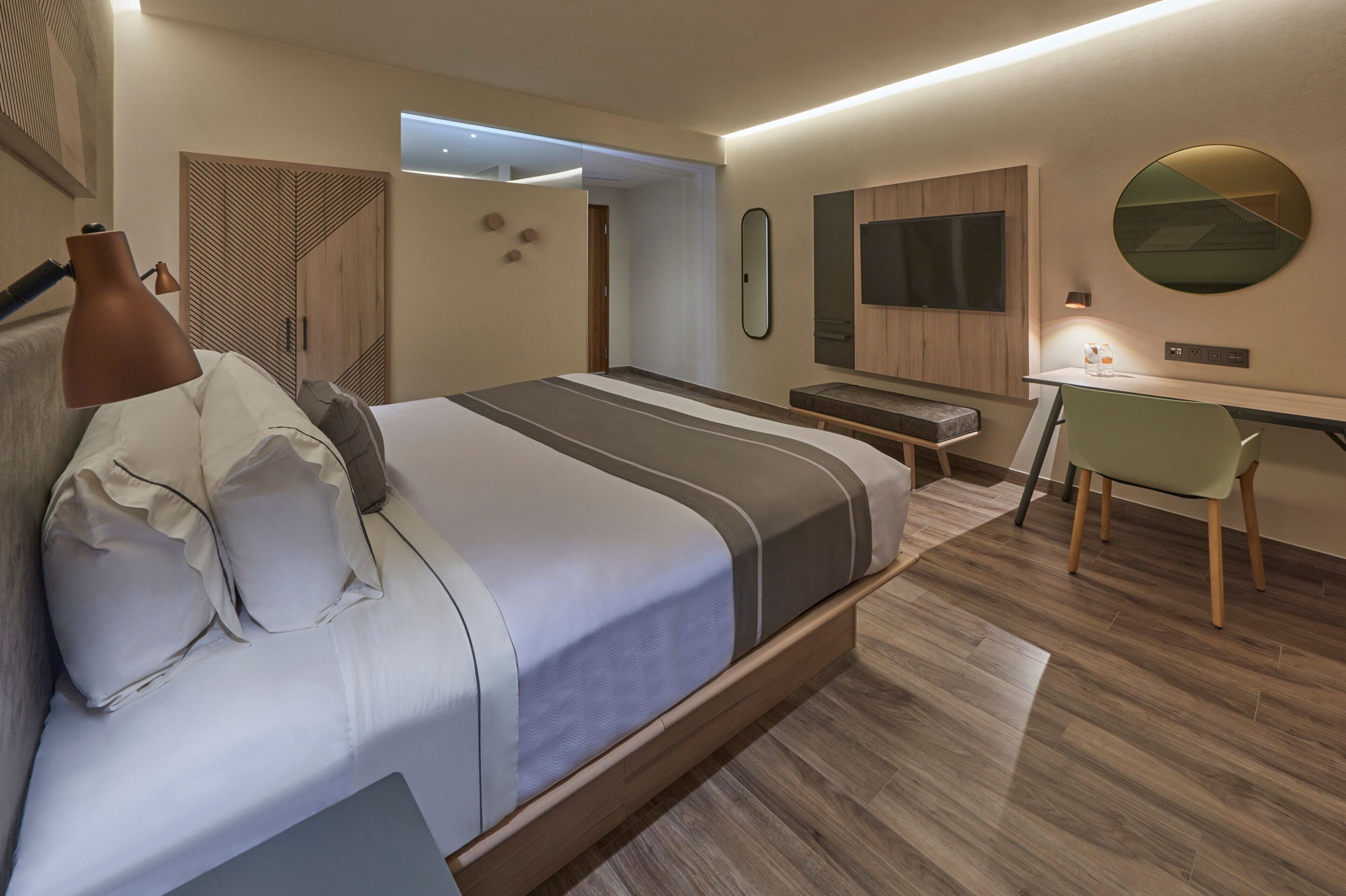 A modern bedroom with a bed, bedside table, lamp, and a desk with a chair.
