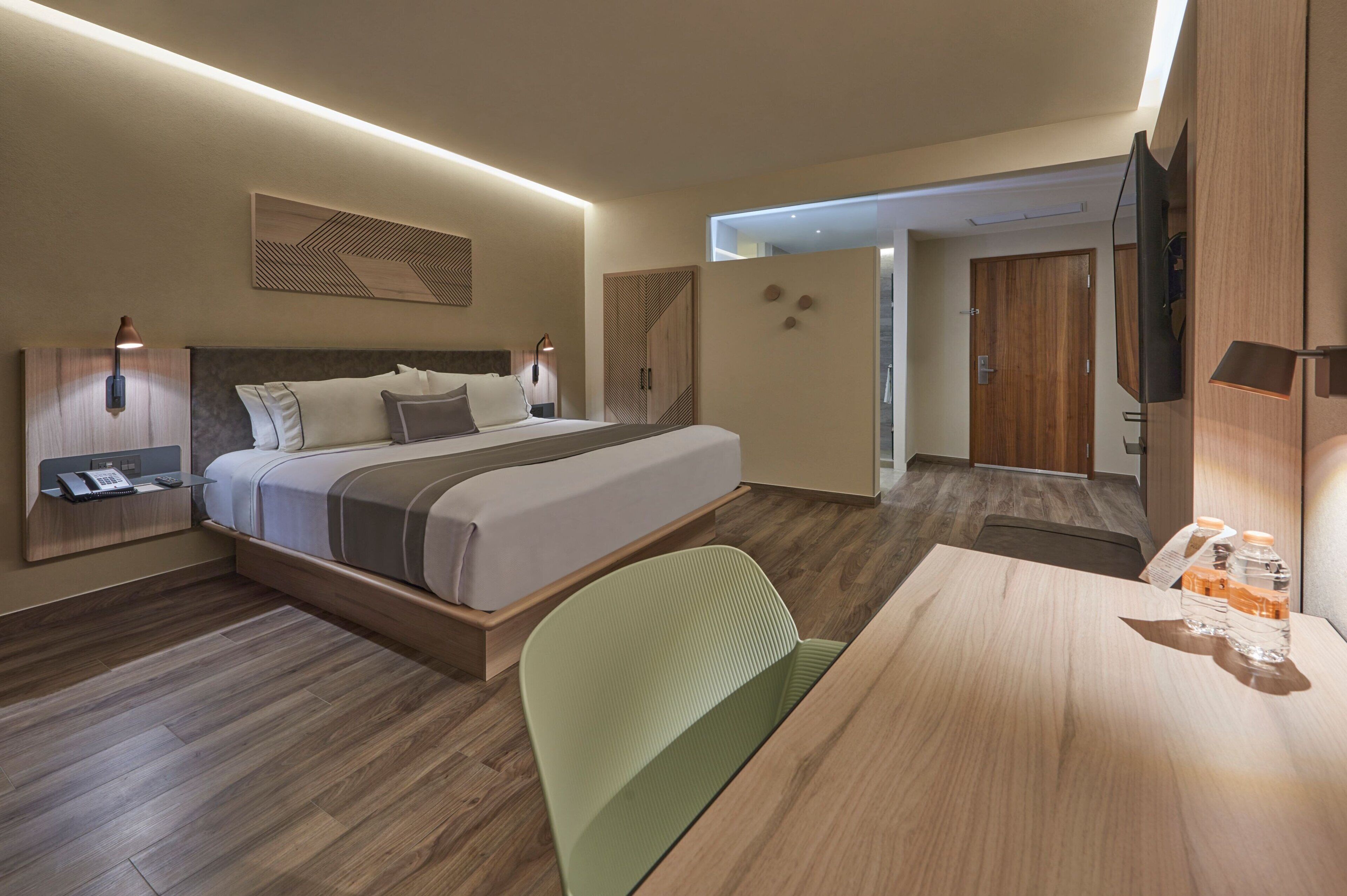Ein modernes Hotelzimmer mit Bett, Nachttisch, Lampe und Fernseher.