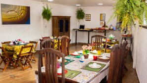 A dining area with wooden chairs and tables, a laptop on a stand, and potted plants.