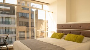 A modern hotel room with a large bed, a view of the city through floor-to-ceiling windows, and a balcony with a chair. - Hotel Wess Bogota (Bogotá)