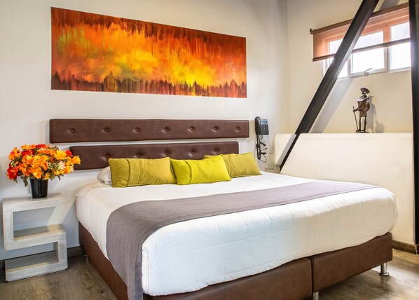 Un dormitorio con una cama grande, un cabecero, una mesita de noche con un florero y un cuadro en la pared.