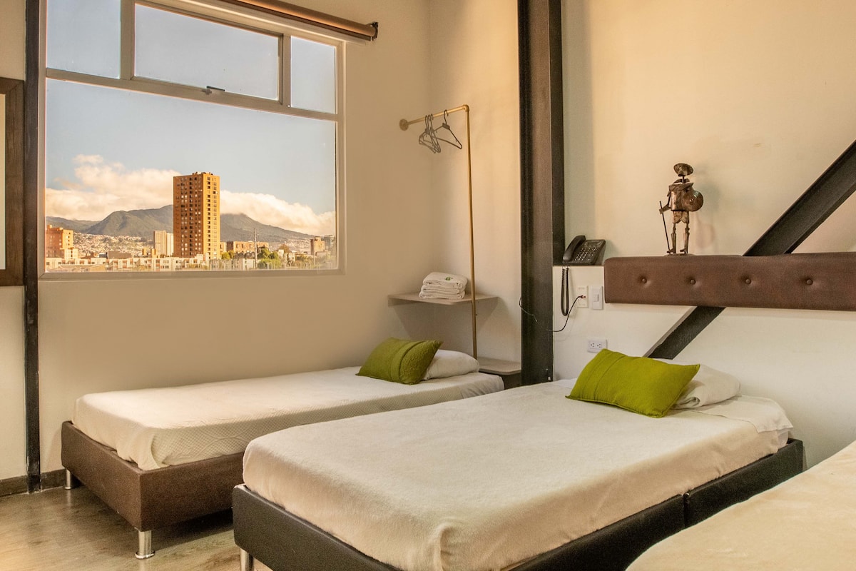 Habitación de hotel con dos camas, una ventana que ofrece vistas a la ciudad, un teléfono y un estante pequeño con una toalla.