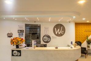 A reception area with a curved counter, a large 'We' logo, and various informational posters. - Hotel Wess Bogota (Bogotá)