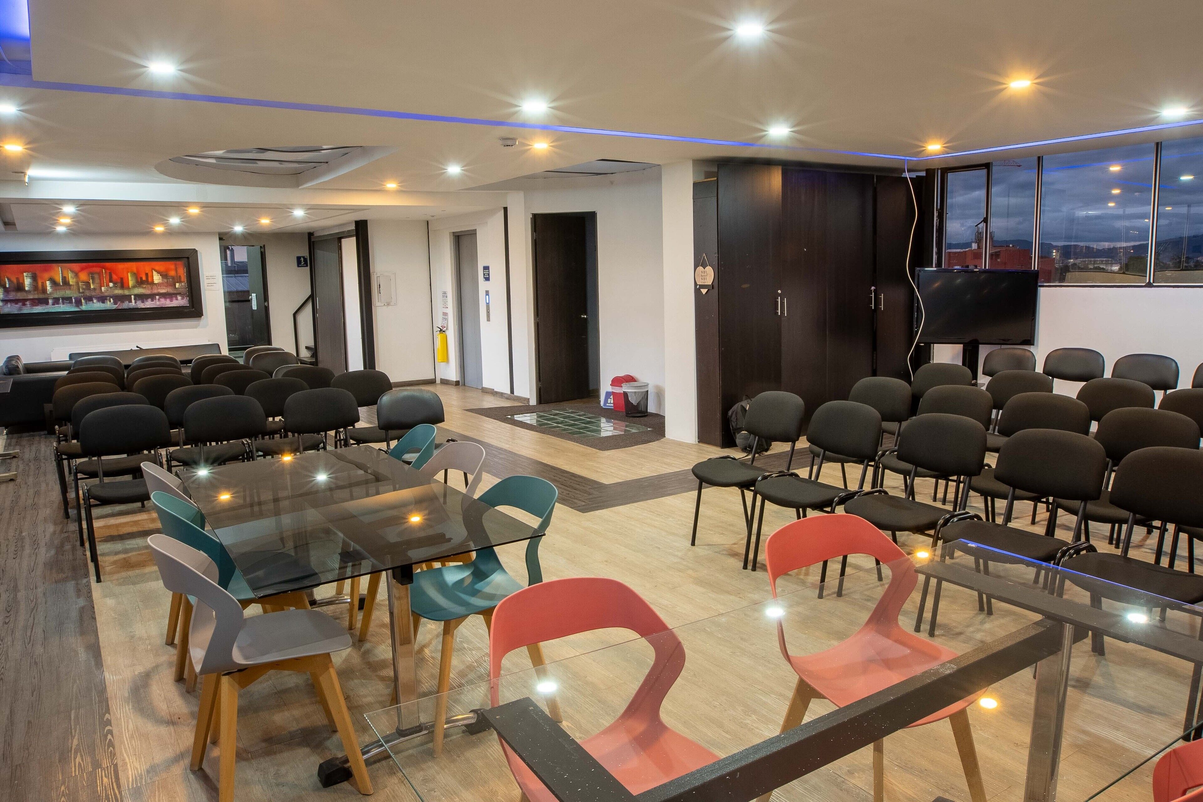 A conference room with glass tables and chairs, a flat-screen TV, and a view of the city through large windows.