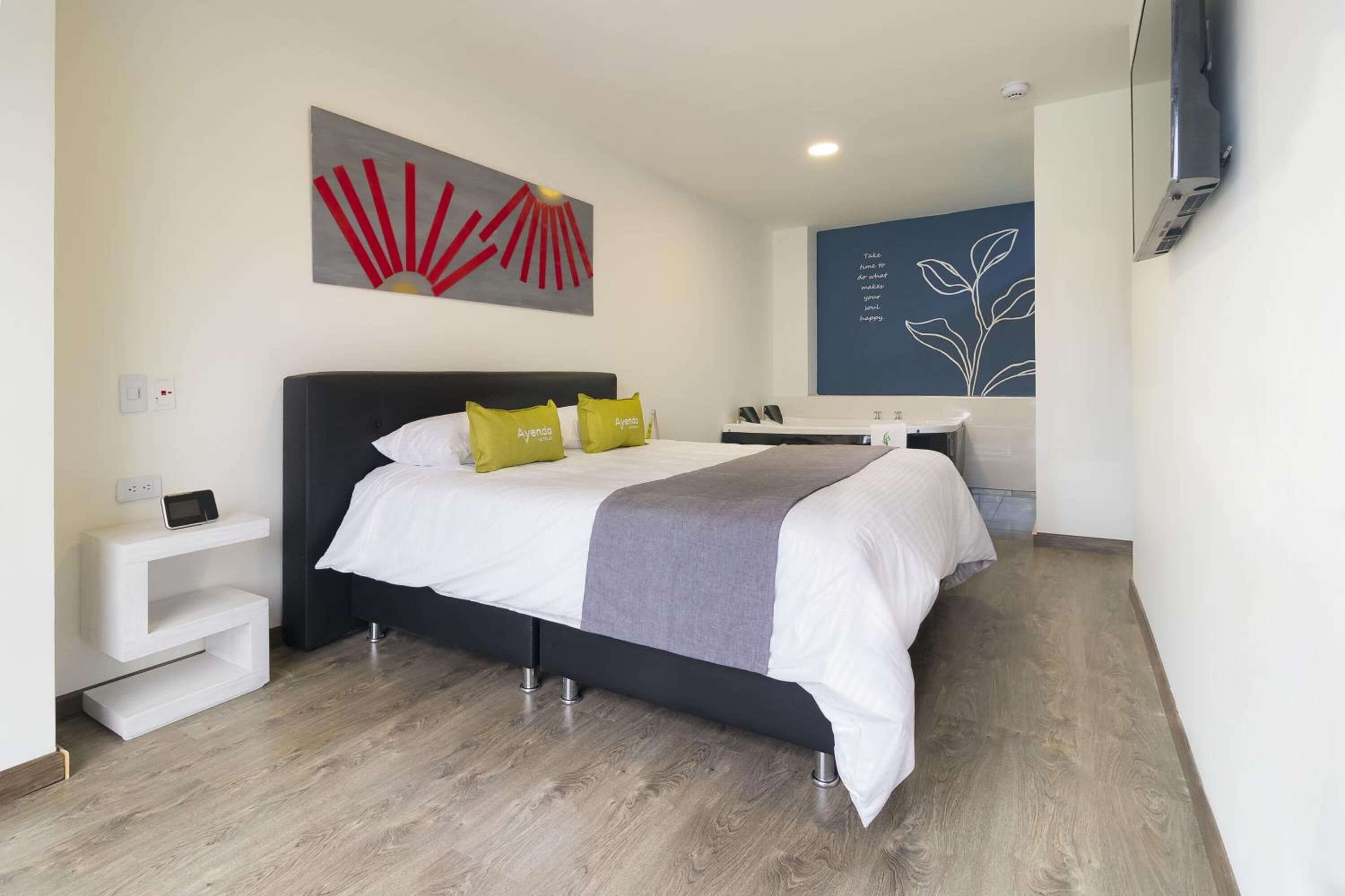 A modern hotel room with a large bed, a bedside table with a phone, and a wall-mounted TV.