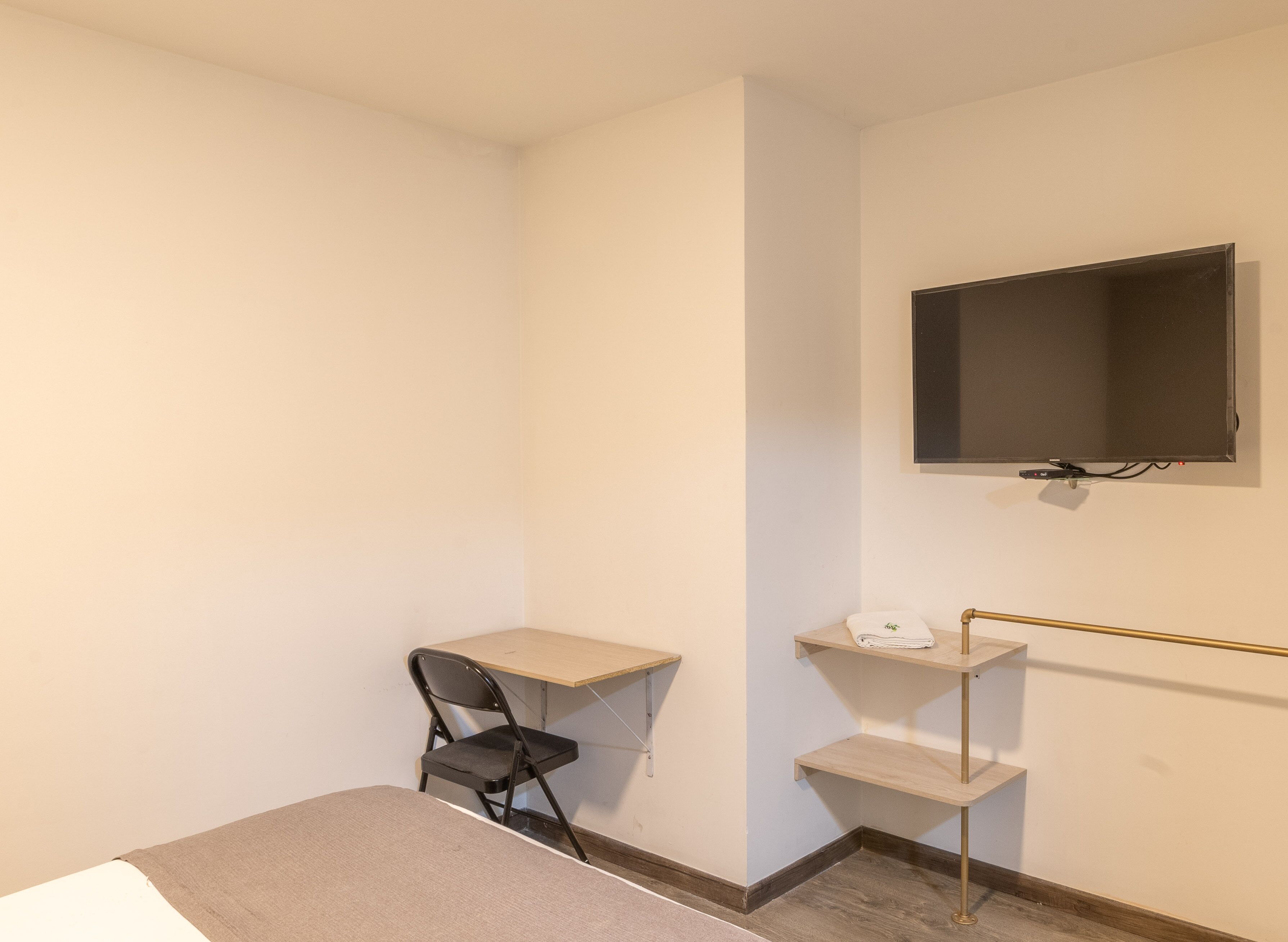 A small, sparsely furnished room with a desk, chair, and a TV mounted on the wall.