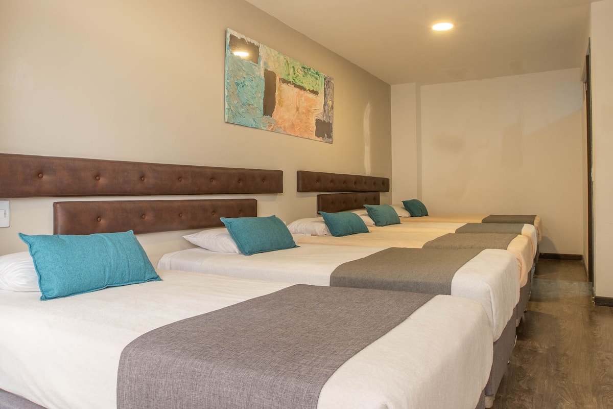 Una habitación de hotel con cuatro camas, cada una con cabecero marrón y almohadas turquesa.