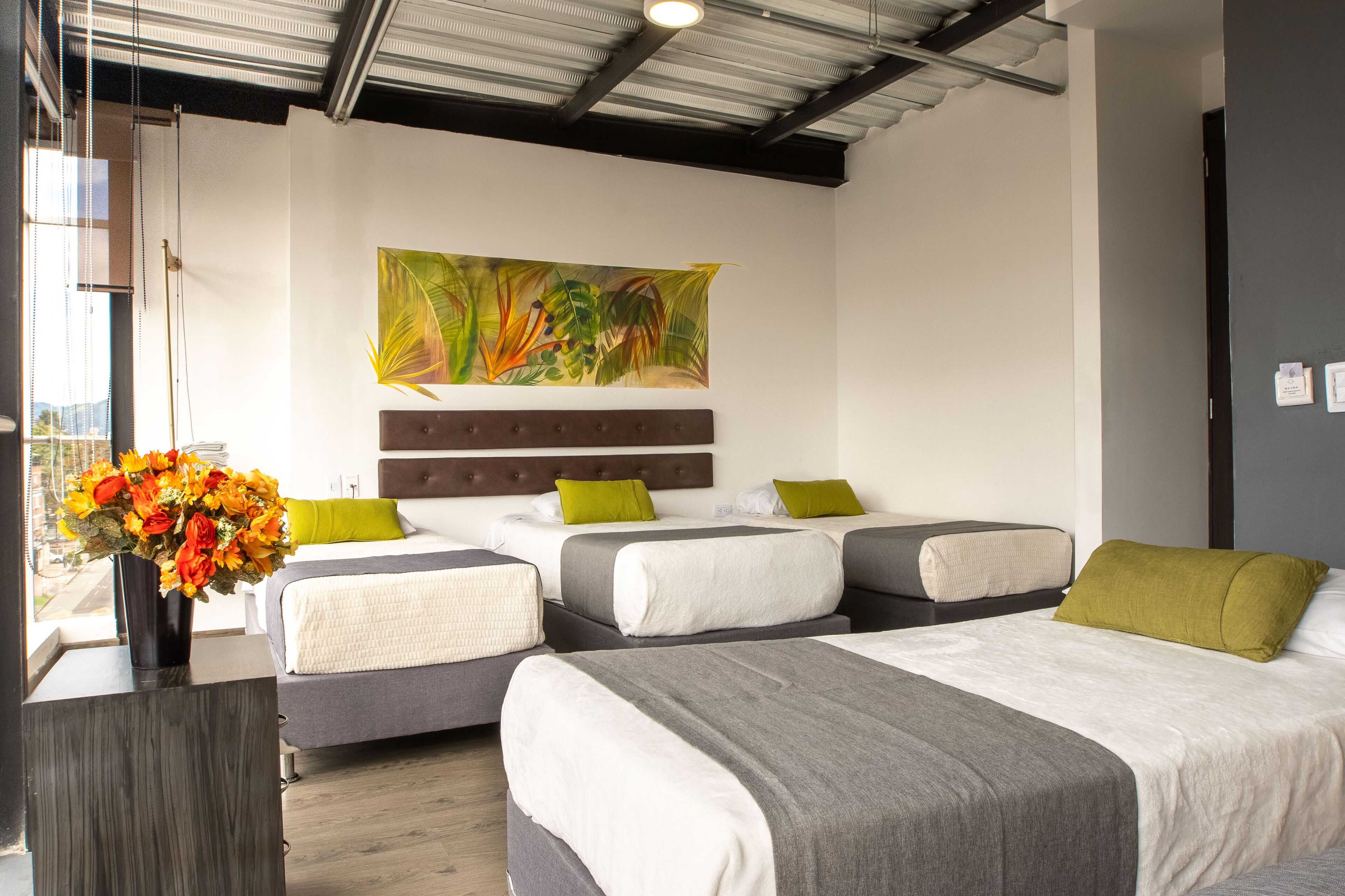 A hotel room with three beds, a large painting, and a vase of flowers.