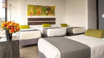 Habitación de hotel con dos camas, un ventanal grande, un cuadro decorativo en la pared y un florero con flores.