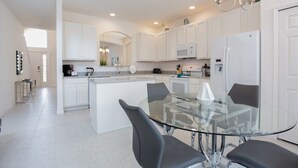 Una cocina moderna con armarios blancos, una mesa de comedor de vidrio y sillas negras.