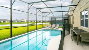 Una piscina al aire libre techada con sillas de descanso y una mesa, rodeada por un recinto de vidrio.