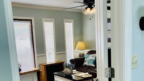 A room with a ceiling fan, a table with a vase, and a bench.
