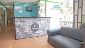 A hotel reception area with a stone reception desk, a grey sofa, and a view of the outside. - Ayenda 1609 Hotel Arrecife Caribeño (Santa Marta)