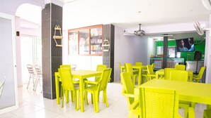 A brightly lit dining area with yellow tables and chairs, a large window, and a television screen. - Ayenda 1609 Hotel Arrecife Caribeño (Santa Marta)