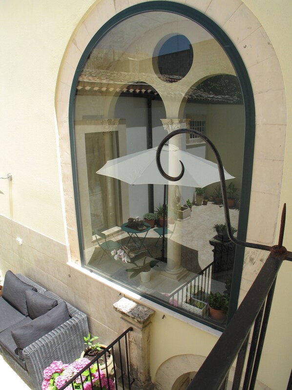 A balcony with a wicker sofa, a potted plant, and a white umbrella.
