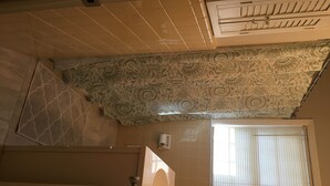 Habitación con techo estampado, pared con azulejos, ventana con persianas y puerta con manija.