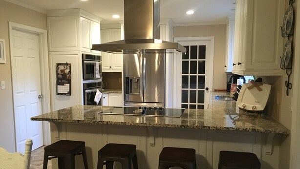Una cocina con una isla central, taburetes de bar, electrodomésticos de acero inoxidable y armarios blancos.