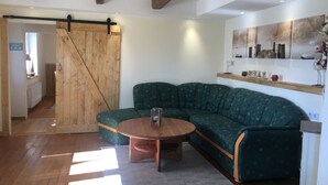 A cozy living room with a green sectional sofa, a wooden coffee table, and a barn-style sliding door. - Restored Gulfhof in the heart of East Frisia (Ihlow)