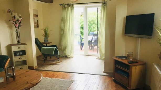 A cozy living room with a wooden floor, a green chair, a small table, a TV, and a sliding glass door leading to an outdoor area. - Restored Gulfhof in the heart of East Frisia (Ihlow)