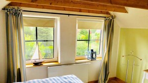 A bedroom with a bed, two windows, a radiator, a small sailboat model, and a coat rack. - Restored Gulfhof in the heart of East Frisia (Ihlow)