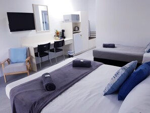 A hotel room with two beds, a desk, a chair, a microwave, and a refrigerator.
