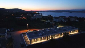 Un edificio moderno con techo plano, rodeado de un estacionamiento y una masa de agua al fondo.