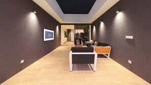 Un couloir moderne avec un luminaire au plafond, un tableau encadré au mur et un coin salon comprenant une table et des coussins.