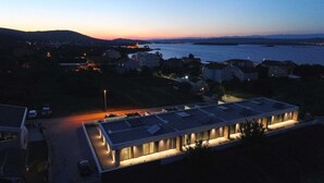 Un bâtiment moderne doté d’un toit plat, entouré d’un parking et avec une étendue d’eau en arrière-plan.